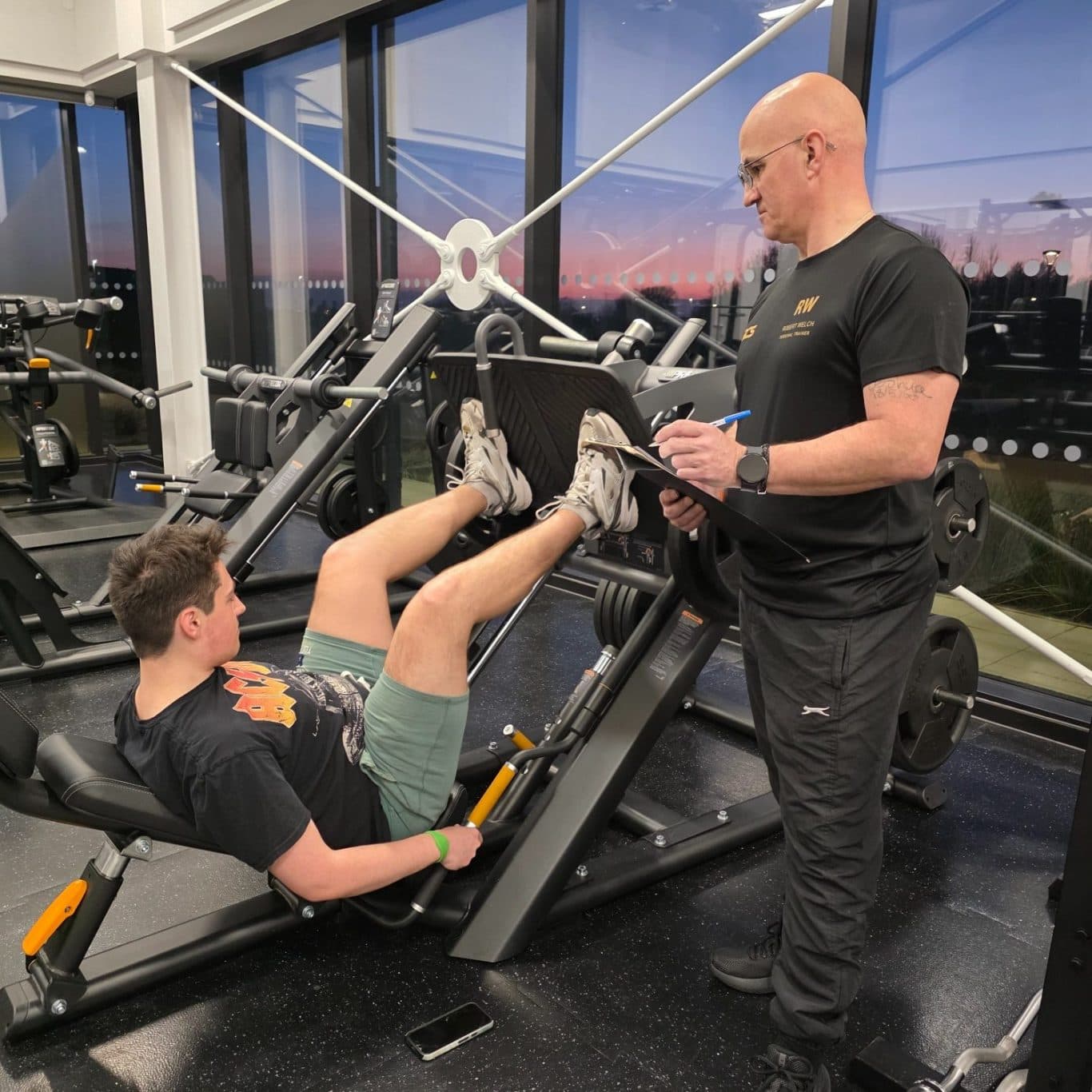 Rob Welch coaching a client on the leg press at the gym